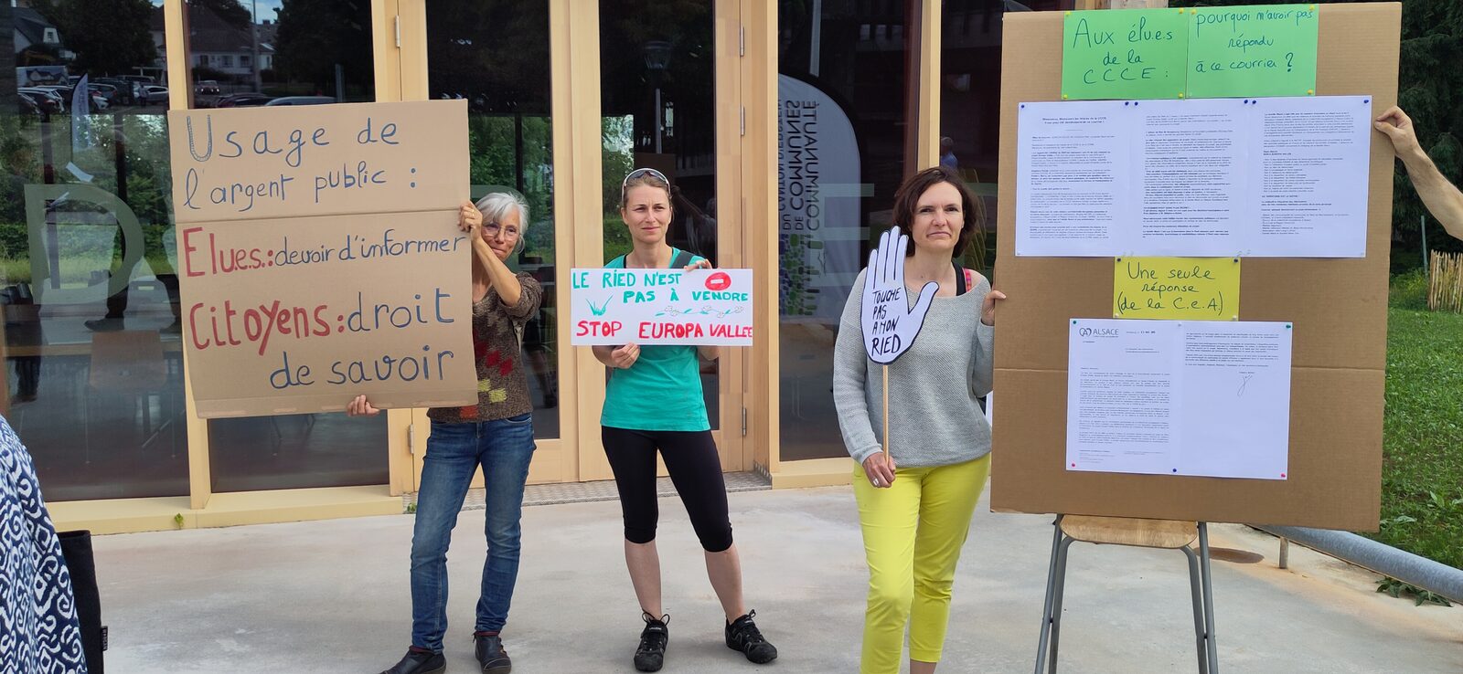 Trois militantes tiennent les pancartes « Usage de l'argent public », « Le Ried n'est pas à vendre » et « Touche pas à mon Ried »